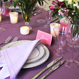 Elegant table setting with purple tablecloth, floral centerpieces, and silverware.