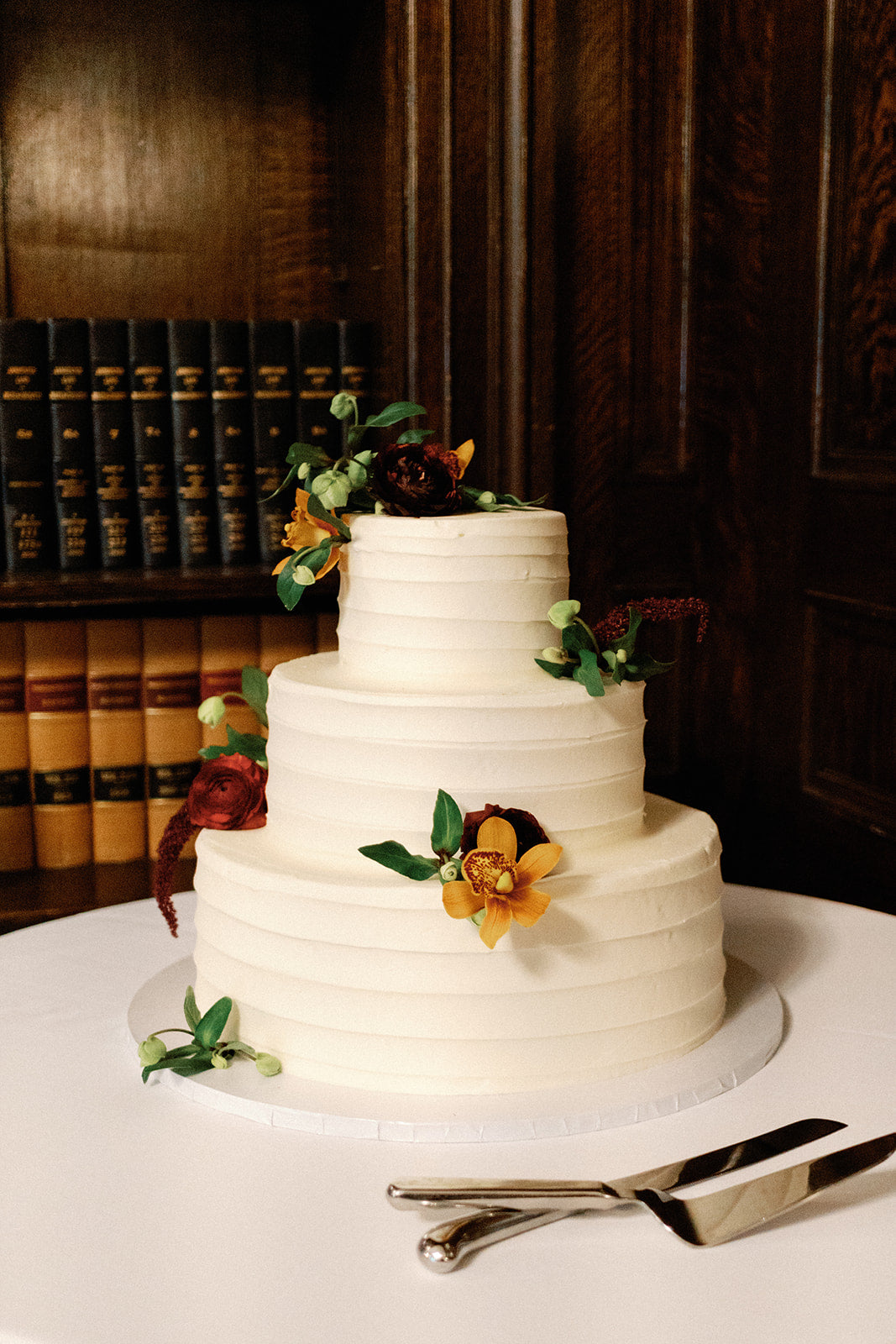Wedding cake with dark and moody flowers in library at North Shore wedding venue.