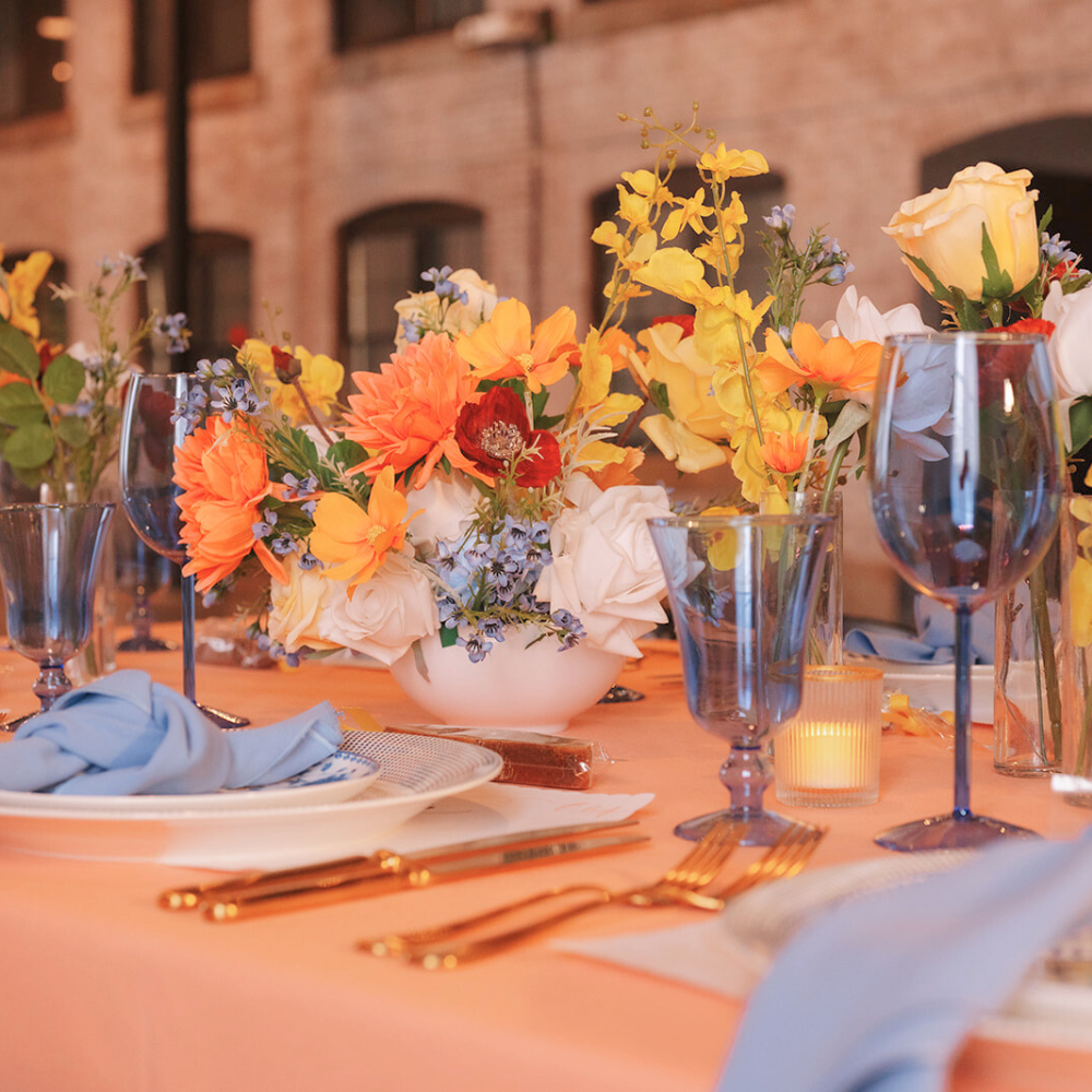 Decorative table setting with floral arrangements, glasses, and cutlery in an indoor setting. With Blue dot charger and floral dinnerware rentals. New England party tablescape.