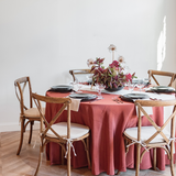 Dining table set with a copper bengaline tablecloth and flax linen rentals, plates, glasses, and a sculptural floral centerpiece.