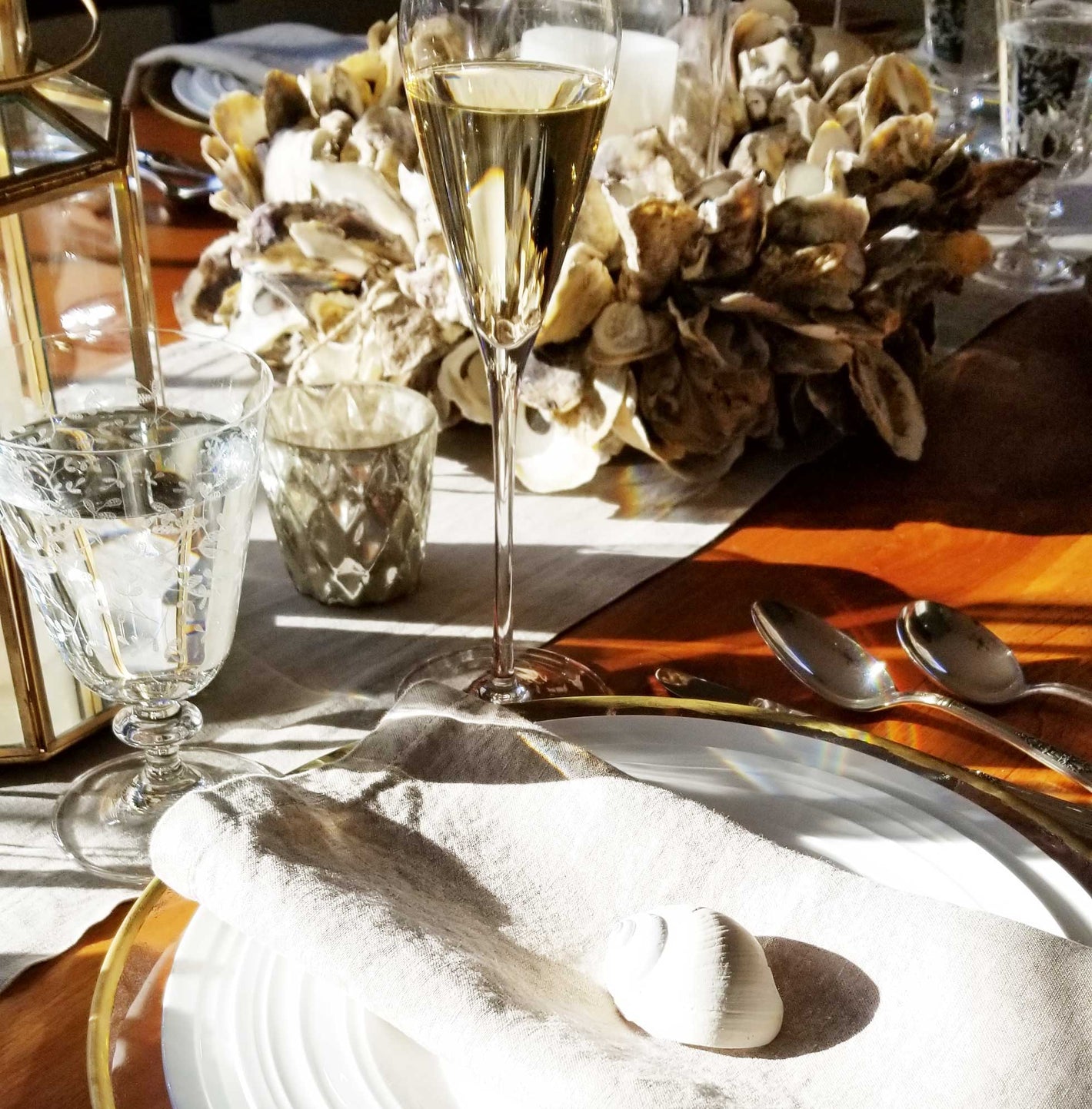 Elegant table setting with champagne glass, silverware, and decorative elements including a gold rimmed charger on a wooden table for a seaside RI event.